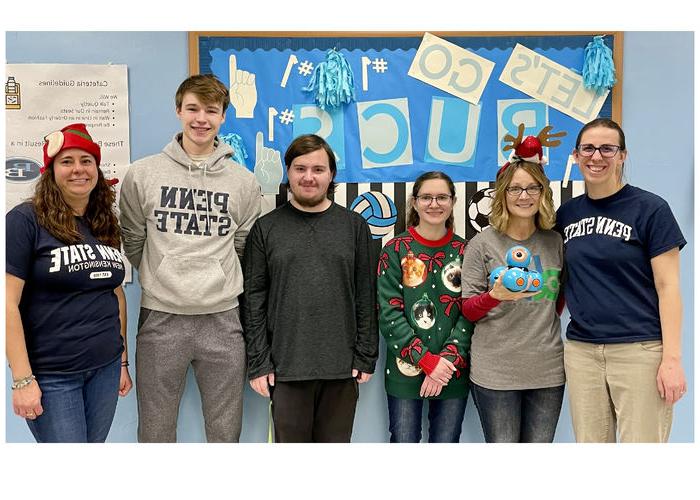 Students and faculty members stand in front of bulletin board for photo